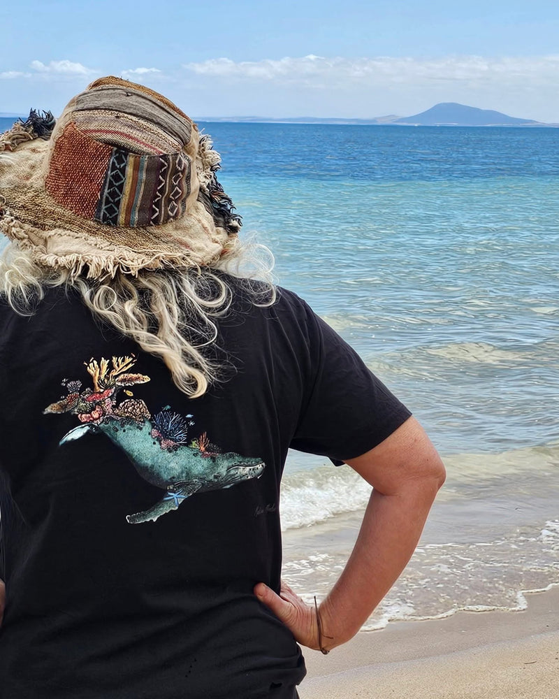 Person wearing a black t-shirt with a whale design on a beach