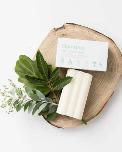 Bar of soap and a box on a wooden plate with green leaves on a white background