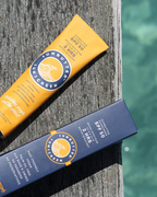 Two bottles of sunscreen on a wooden post with water in the background