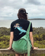 Person sitting on a wooden railing overlooking a scenic landscape with trees and water.