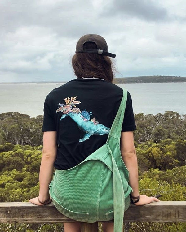 Person sitting on a wooden railing overlooking a scenic landscape with trees and water.
